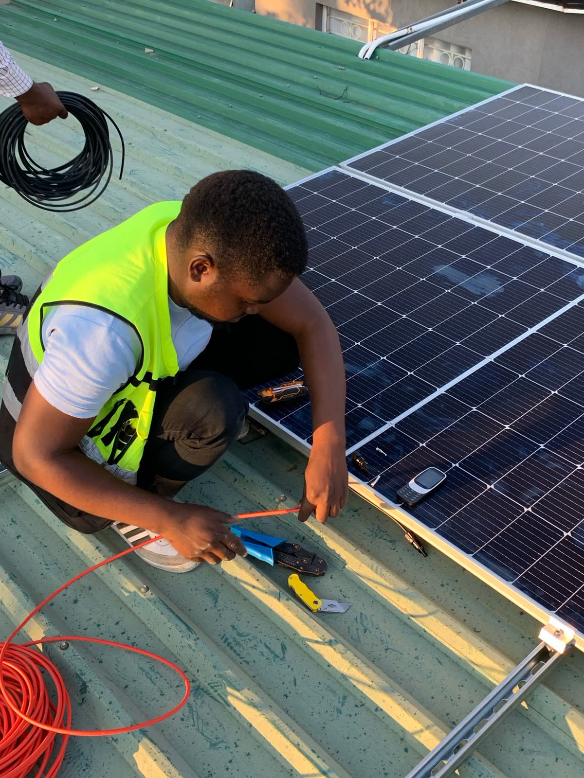 Técnico de colete refletivo fazendo a ligação dos cabos de uma placa solar no telhado