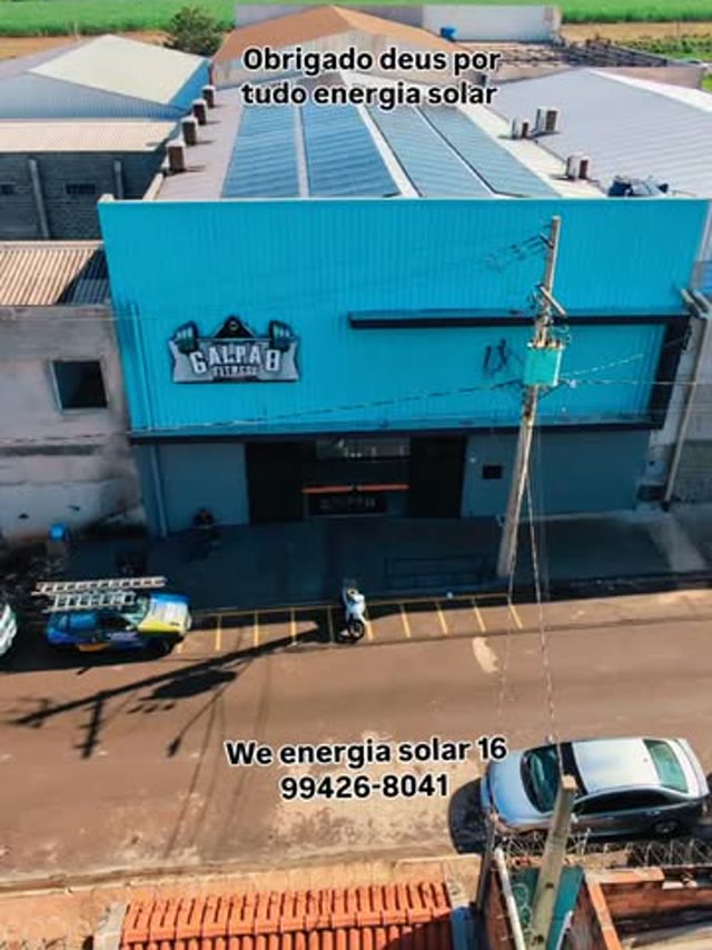 Vista aérea de um galpão azul com o telhado coberto de placas solares
