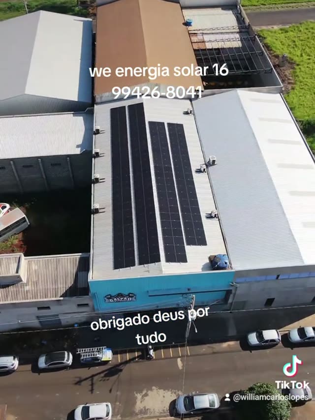 Vista aérea de um barracão à beira de uma rodovia com fileiras de placas solares no telhado