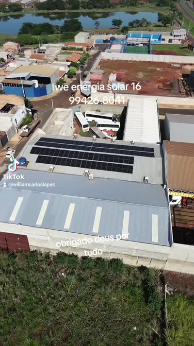 Vista de drone de um galpão de telhado metálico com três fileiras de placas solares